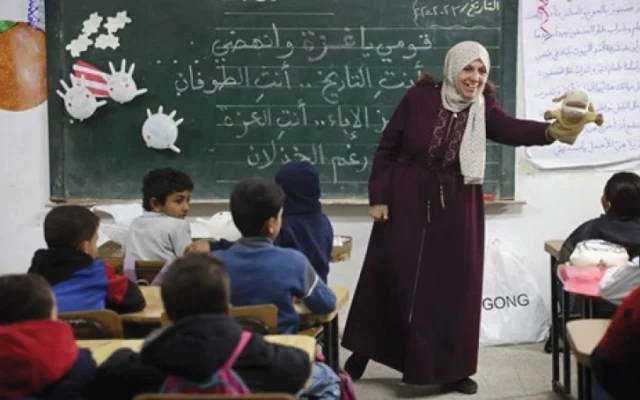 Une enseignante de l'école élémentaire Al-Nasr, dans la ville de Gaza, à côté d'un tableau noir sur lequel on peut lire « Vous êtes le Toufan » (le déluge), une allusion au Déluge d'al-Aqsa, le nom donné par le Hamas au pogrom du 7 octobre 2023 perpétré dans le sud d’Israël, le 23 février 2025. (Crédit : Omar AL-QATTAA / AFP)