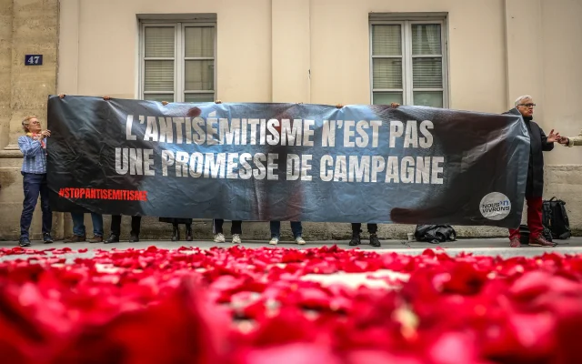 Illustration : Des manifestants hissant une banderole sur laquelle on peut lire "L'antisémitisme n'est pas une promesse de campagne" à l'entrée d'une conférence de presse au cours de laquelle les dirigeants français de gauche ont annoncé qu'ils formaient une alliance appelée le nouveau Front populaire, à Paris, en France, le 14 juin 2024. (Crédit : Thomas Padilla/AP)