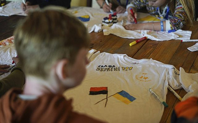 Un garçon décore un t-shirt avec les mots « Gloire à l'Ukraine » dans un camp de réadaptation pour enfants et mères victimes de la guerre près de Lviv, en Ukraine, le mercredi 3 mai 2023. Les enfants reçoivent des t-shirts blancs et sont invités à exprimer leurs sentiments par le dessin. Toute une génération d'enfants ukrainiens a vu sa vie bouleversée par l'invasion de leur pays par la Russie. Des centaines d'enfants ont été tués. Pour les survivants, ce traumatisme profond laissera des séquelles psychologiques qui les suivront à l'adolescence et à l'âge adulte. L'UNICEF estime qu'environ 1,5 million d'enfants ukrainiens sont exposés à des risques de troubles mentaux. (Crédit : AP/Hanna Arhirova)