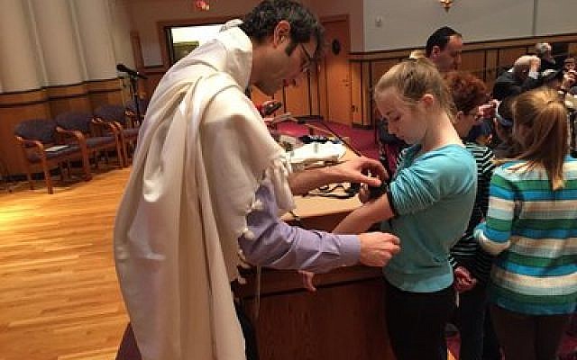 Rabbi Seth Adelson of Congregation Beth Shalom is laying tefillin on a J-JEP student. Photo courtesy of J-JEP