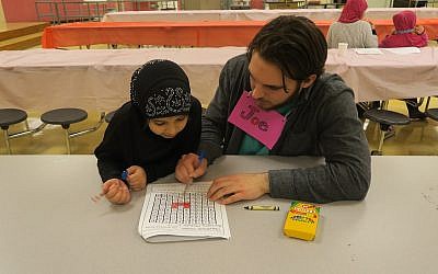 A JFCS volunteer helps Syrian native Aisha complete her homework. (Photo courtesy of JFCS)