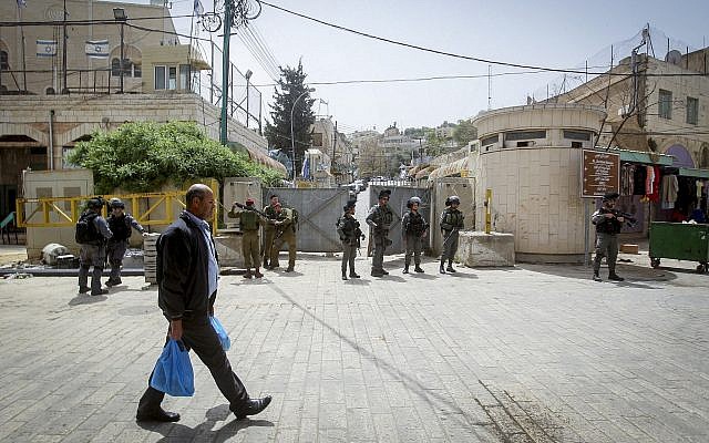 A Palestinian man walks by Israeli troops standing guard in the West Bank city of Hebron. (Photo by Wisam Hashlamoun/Flash90)