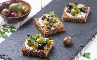 Rye bread toast (canape) with black and green olives, feta cheese and parsley. Tasty snack for gourmets on a slate plate. Selective focus
