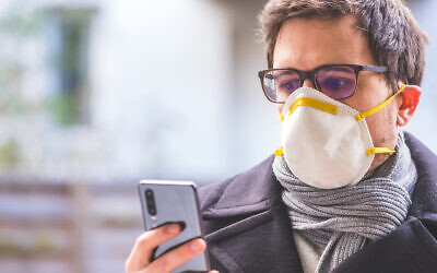Young business man outdoors with a breathing mask and smartphone. Flue and corona season. Photo by Patrick Daxenbichler/iStockphoto.com