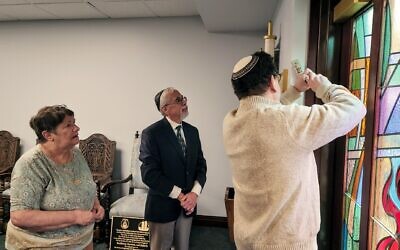 Co-presidents Barbara Caplan and Stephen Cohen watch Rabbi Jonathan Perlman affix the mezuzah to New Light Memorial Chapel's doorpost. Photo by Adam Reinherz