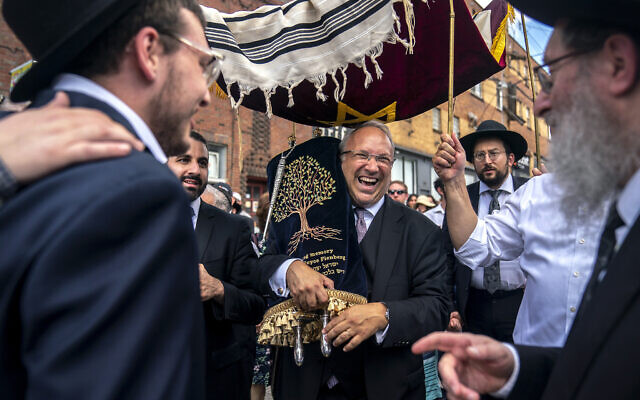 Anthony Fienberg laughs with other members of the community as he carries the new Torah dedicated to his parents Joyce Fienberg, one of the 11 victims of the Tree of Life synagogue shooting, and Dr. Stephen Fienberg, during a procession down Murray Avenue from Beacon Street to Shaare Torah Congregation in Squirrel Hill to celebrate the completion of the Torah, Sunday, July 30, 2023. (Alexandra Wimley/Pittsburgh Union Progress)