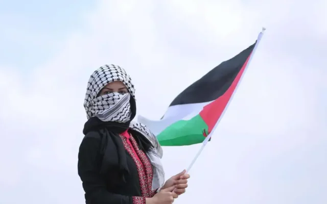 A woman wearing a keffiyeh and holding a Palestinian flag. (Credit: hosnysalah/Pixabay)