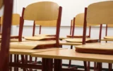 Chairs propped up on desks in an empty classroom. (Credit: Taken/Pixabay)