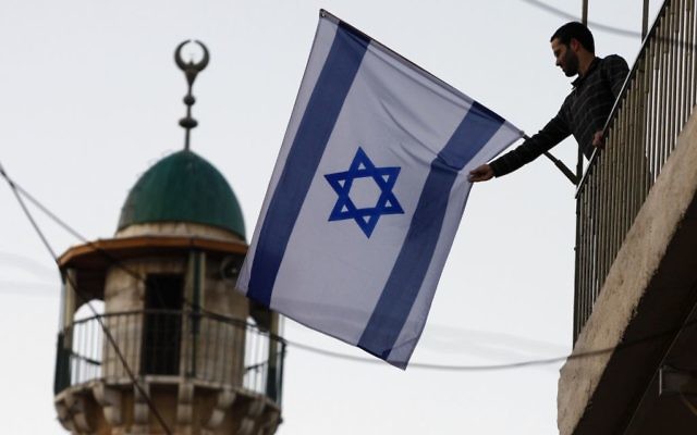 An Israeli Jews raises a flag near the Old City of Jerusalem. The number of Jewish residents in the Old City and predominantly Arab areas nearby has increased 40 percent since 2009. (Abir Sultan/Flash 90)