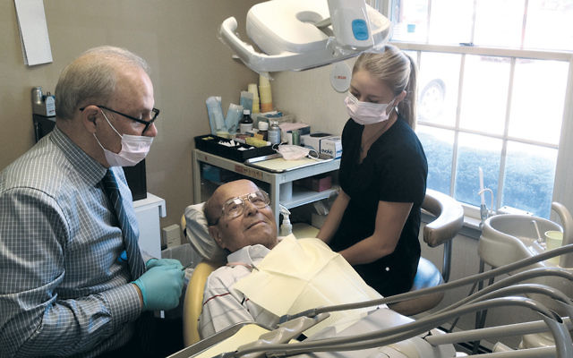 Dr. Michael Goldberg, a dentist and the volunteer dental liaison to the DASH program, and assistant Amanda Lutz flank a survivor, who lives in Fair Lawn and chooses not to reveal his name. “He went through several concentration camps; he is very grateful for the DASH services provided, and he told his social worker he smiles more,” social worker Alice Bass said. (Jewish Family Services of North Jersey)