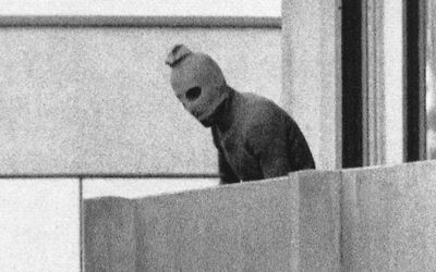 A Black September terrorist looks out from a terrace; the doomed Israelis athletes are held hostage in the apartment behind him.