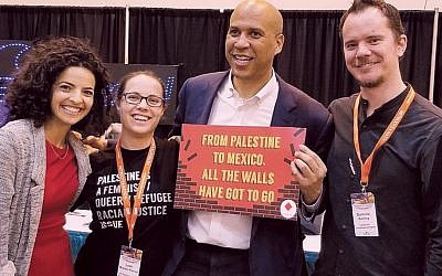 Senator Cory Booker holds an anti-Israel sign after delivering a speech and being asked for a photo by pro-Palestinian activists.