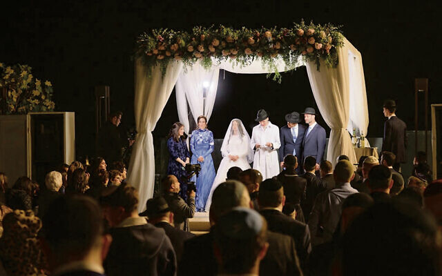 Dov Betzalel and Kayla stand together under the chuppah; Dov Betzalel’s zaidie’s tallit is above them.