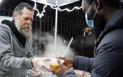 A volunteer, left, distributes hot soup at a distribution tent set up by the Masbia kosher pantry network near the scene of a deadly fire in the Bronx, Jan. 10, 2022. The fire, which claimed 19 lives, is the city’s deadliest in 30 years. (Courtesy Masbia)