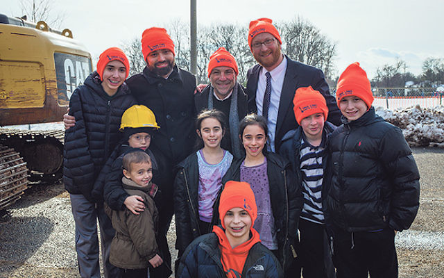 At the demolition site, Torah Links of Middlesex County president Dr. Steve Reich, center, and codirectors Rabbis Shlomo Landau, left, and Dovid Gross are joined in celebration by young people, many wearing the orange ski caps given out by the organizatio