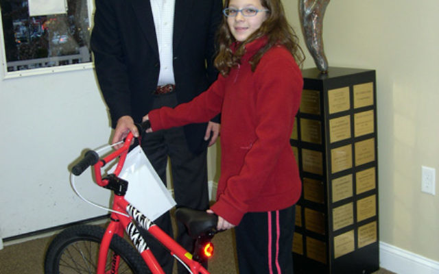 Lillia Shub presents the bicycle she won in a shul raffle to JFS executive director Tom Beck, to be given to a needy child. Photo courtesy of JFS