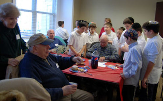 Boys from the JEC, who came to sing for seniors at a JFS Hanukka party, gather around Dave Lefkovic as he makes them paper airplanes. Looking on are Shirley and Moshe Rosenthal.