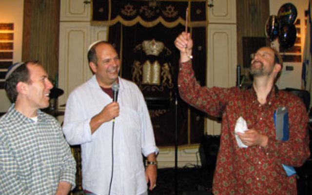 At his installation ceremony at the Sixth Street Community Synagogue, Rabbi Greg Wall holds aloft the silver yad he received from congregation president David Landis, left, and chairman Matthew Pace.