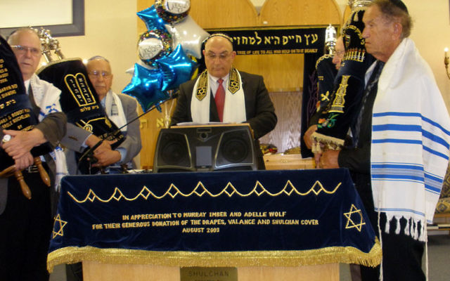 Cantor Eli Perlman leads a service celebrating the renaming of Congregation Beit Shalom, surrounded by synagogue members holding Torah scrolls.