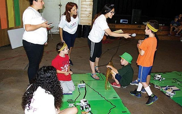 Youngsters at NJ Y Camps learn how to maneuver their robot cars on the map of Israel — as they answer questions about the country in order to proceed — with, from left, Shahaf Pinion, robotics teacher from ORT Kadima Mada in Dimona; Ayelet Abramovitch, chief of informal education at ORT Kadima Mada; and Ziv Itzhak and, in foreground, Ta’ir David, both from ORT Kadima Mada in Dimona.