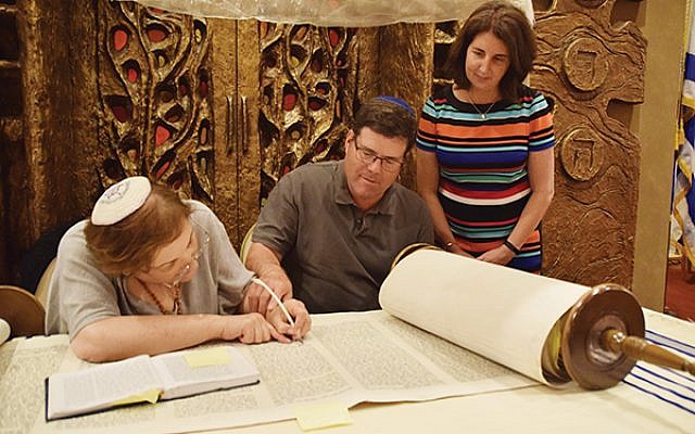 Scott Borsack lays his hand on the hand of soferet Linda Coppleson as she inscribes words as part of her repair work on the Torah scroll at the Jewish Center; his wife, Charlene, awaits her turn. Photo by Talya Feldman