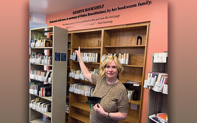 Ms. Kook stands at the Teaneck library’s reserve section, near the sign in memory of Helen Brueckheimer.
