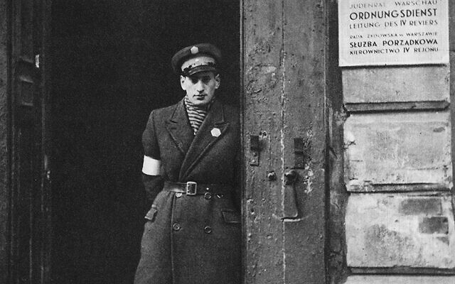 A Jewish policeman stands at the entrance of a Warsaw ghetto police station. (Wikipedia)