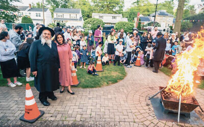Rabbi Mordechai and Shterney Kanelsky stand in front of the bonfire; there is a crowd behind them. (Courtesy BA)