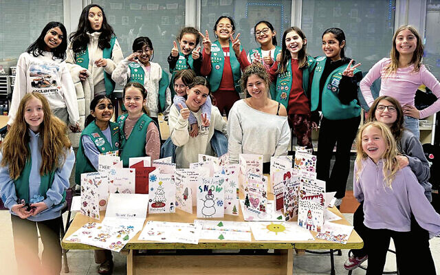 Maddie Rost, founder of Signed With a Smile, at front in off-shoulder sweatshirt, creating cards with a local Girl Scout troop. Maddie Rost, founder of Signed With a Smile, at front in off-shoulder sweatshirt, creating cards with a local Girl Scout troop.