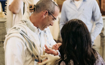 Rabbi Hayim Leiter cradles a baby during a bris. (Photo by Tzvety Friedman)