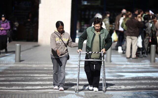 Illustrative: A carer helping an elderly Israeli to cross the street in Tel Aviv. (Kobi Gideon/Flash90)