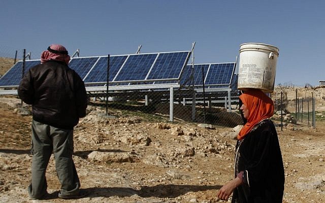 A Palestinian woman carries a bucket of water next to solar panels in Al-Thala. (photo credit: AP/Majdi Mohammed)