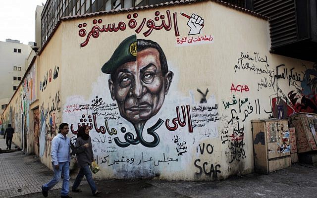An Egyptian couple walks past a mural depicting military ruler Field Marshal Hussein Tantawi on the left side of the face and ousted president Hosni Mubarak on the right side, with Arabic that reads, 'Who assigned you did not die, No for gas export to Israel, the revolution continues,' at Tahrir Square in Cairo. (photo credit: AP/Nasser Nasser)