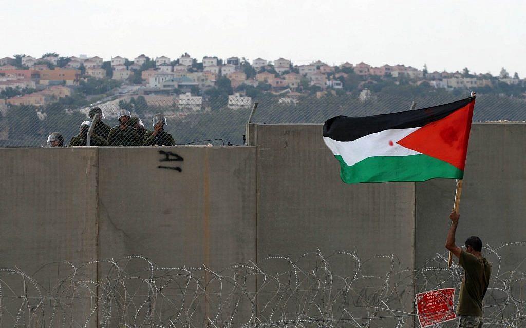 A Palestinian protester holds a flag as he stands near the security fence during a protest in Bil'in in September, 2011 (photo credit: Issam Rimawi/Flash90)