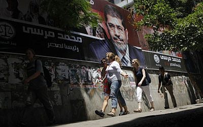 Wisatawan berjalan melewati poster kampanye yang mendukung calon presiden Mesir Mohammed Morsi di Kairo (kredit foto: AP Photo/Amr Nabil)
