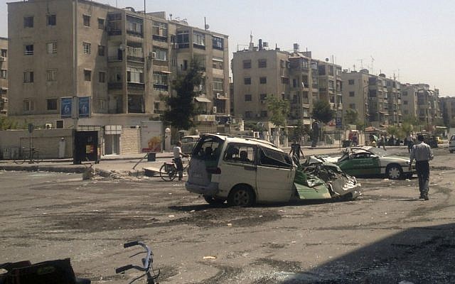 Civilians walk past vehicles destroyed by fighting between rebels and Syrian troops in the Yarmouk camp for Palestinian refugees in south Damascus, Syria, in 2012. (photo credit: AP)