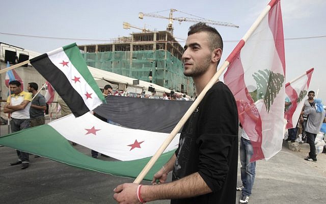 A man carries the Syrian revolutionary flag and a Lebanese national flag, as people gather in Martyrs' Square before the funeral for the country's intelligence chief, Brig. Gen. Wissam al-Hassan in Beirut, Lebanon, Sunday, October 21, 2012 (photo credit: AP Photo/Maya Alleruzzo)