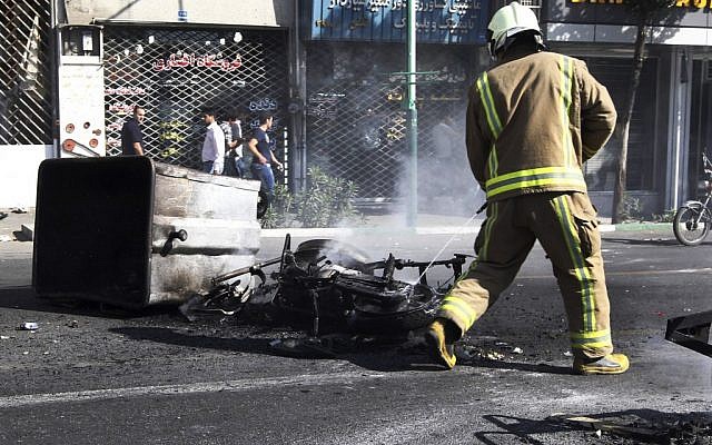 In this photo obtained by the Associated Press, an Iranian fire fighter extinguishes a burned motorcycle in a street in central Tehran, near Tehran's old main bazaar, during currency protests, Wednesday, October 3, 2012. (photo credit: AP)
