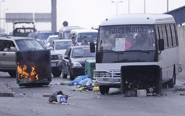 A bus pushes a garbage container used as a roadblock by Sunni protesters after overnight clashes between Sunni and Shiite gunmen in Beirut, Lebanon on Monday. (photo credit/Hussein Malla/AP)