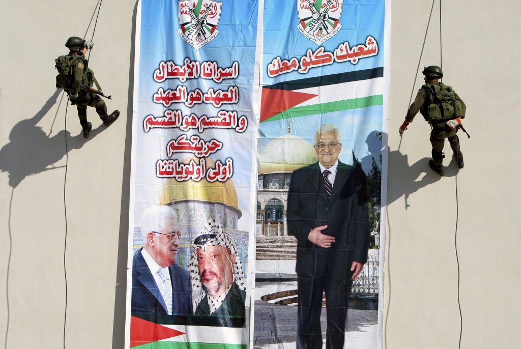 Palestinian security officers slide down a building next to a banner of President Mahmoud Abbas with Yasser Arafat, in the West Bank town of Jenin on Wednesday. Arabic on the left reads "our hero prisoners, the covenant is the covenant and the section is the section, your liberty will stay our first priority," and right, "all your people (are) with you."(photo credit: AP/Mohammed Ballas)