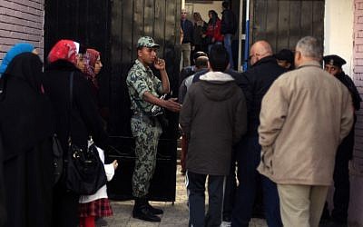 Seorang tentara Mesir menunggu di luar tempat pemungutan suara di Kairo, Mesir, pada hari Sabtu ketika orang-orang mengantri untuk memberikan suara mereka dalam referendum mengenai konstitusi yang disengketakan yang dibuat oleh kelompok Islam pendukung Presiden Mohammed Morsi (kredit foto: AP/Khalil Hamra)