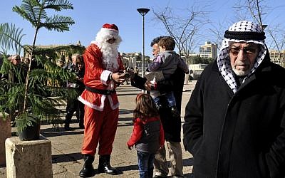 A man dressed as Santa Claus distributes Christmas trees to Christians outside Jaffa Gate in the Old City of Jerusalem on Sunday, Dec. 23, 2012. (photo credit: Mahmoud Ilean/AP)
