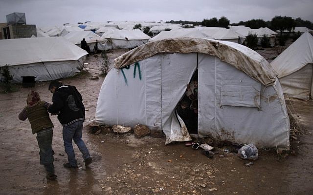 Children, who fled their home with their family, peek from their tent at a man helping a girl, after she fell on slippery ground, at a camp for displaced Syrians, in the village of Atmeh, Syria, Tuesday, Dec. 18, 2012. (photo credit: Muhammed Muheisen/AP)
