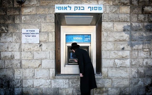 A man removes cash from a Bank Leumi ATM machine in the Meah Shearim neighborhood of Jerusalem (Nati Shohat/Flash90)
