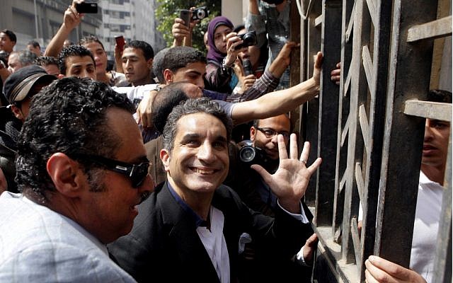 Popular Egyptian television satirist Bassem Youssef, who has come to be known as Egypt's Jon Stewart, waves to supporters as he enters the Egyptian state prosecutor's office in Cairo to face accusations of insulting Islam and the country's Islamist leader, Sunday. Government opponents said the warrant against such a high profile figure, known for lampooning Egyptian President Mohammed Morsi and the new Islamist political class, constituted an escalation in a campaign to intimidate critics. (AP Photo/Amr Nabil)