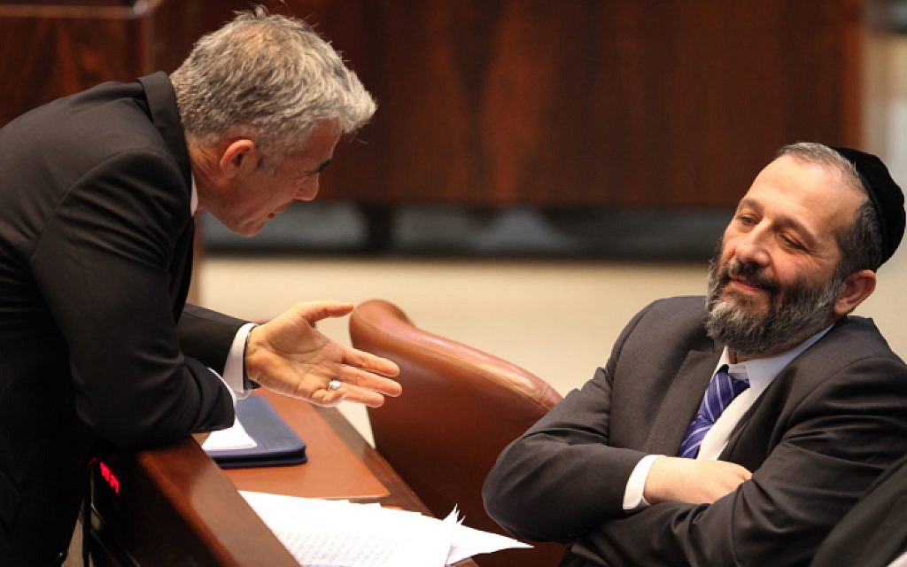 Then-finance minister Yair Lapid, left, talks to Shas chairman Aryeh Deri at the Knesset in March 2013. (Isaac Harari/Flash90)