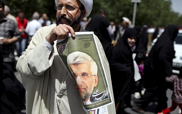 An Iranian cleric holds up a poster of presidential candidate Saeed Jalili, Iran's top nuclear negotiator, after the Friday prayer in Tehran, Friday, May 31, 2013. Iranians have seen it before: A youngish presidential candidate firing up crowds with fist-waving rants against the West, then displaying his Islamist bona fides with courtesy calls to hard-line clerics. (AP Photo/Ebrahim Noroozi)