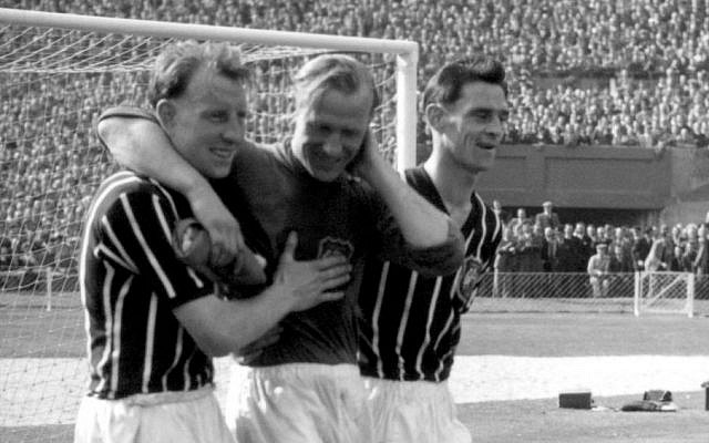 FILE - A May 5, 1956 photo from files of Bernd Trautmann, more commonly known as Bert, Manchester City's German-born goalkeeper, center, being assisted from the pitch by two unidentified players, suffering from a broken neck, during the FA Cup final against Birmingham, at London's Wembley Stadium. (Photo credit: AP/PA, File)