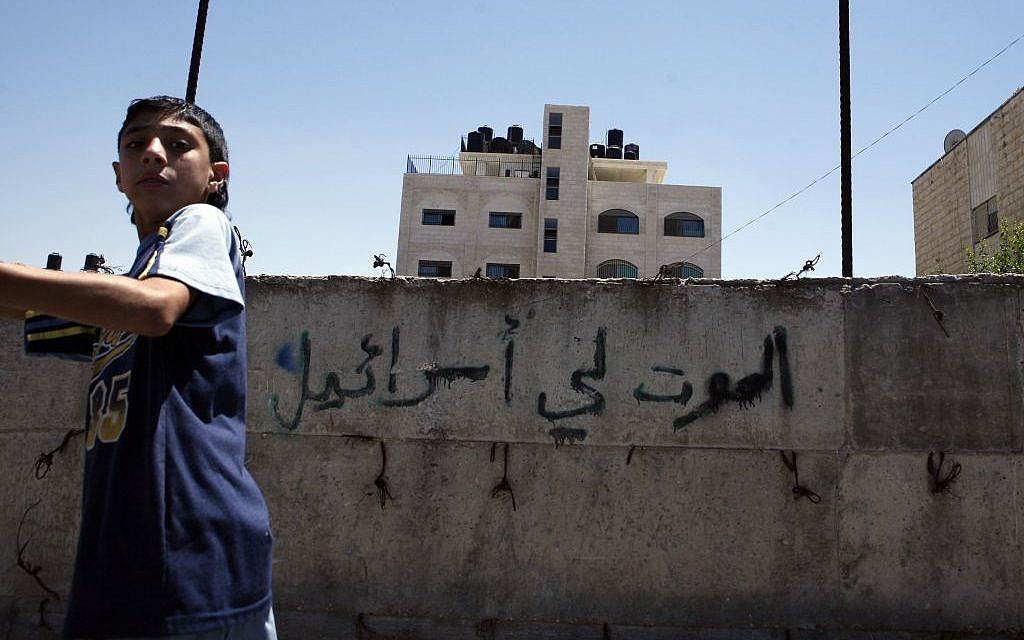 A Palestinian boy walks past a wall painted with graffiti reading 'Death to Israel' in the northern Jerusalem Palestinian neighborhood of Beit Hanina, July 2008 (Michal Fattal/Flash90)