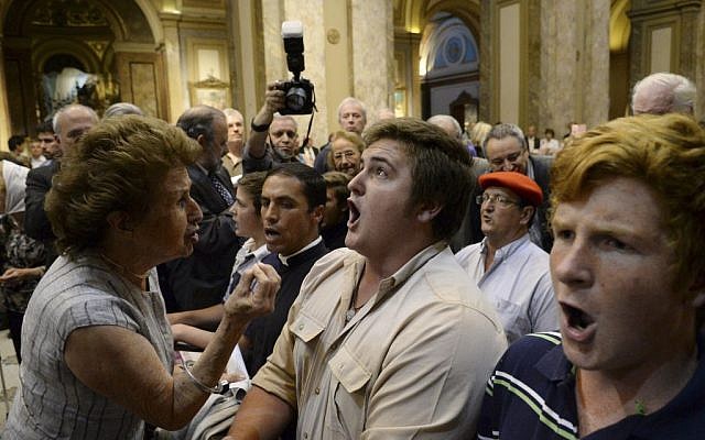 A woman attending a ceremony that marked Kristallnacht and the beginning of the Holocaust, left, tries to stop ultra-traditionalist Catholics from interrupting the interfaith event at the Metropolitan Cathedral in Buenos Aires, Argentina,  Nov. 12, 2013. (photo credit: AP/Rodolfo Pezzoni,DyN)